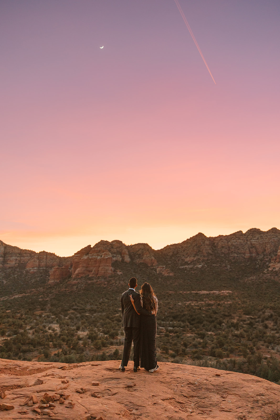 Couple dressed in all black stands together looking into sky at sunset to watch moon and stars begin to shine