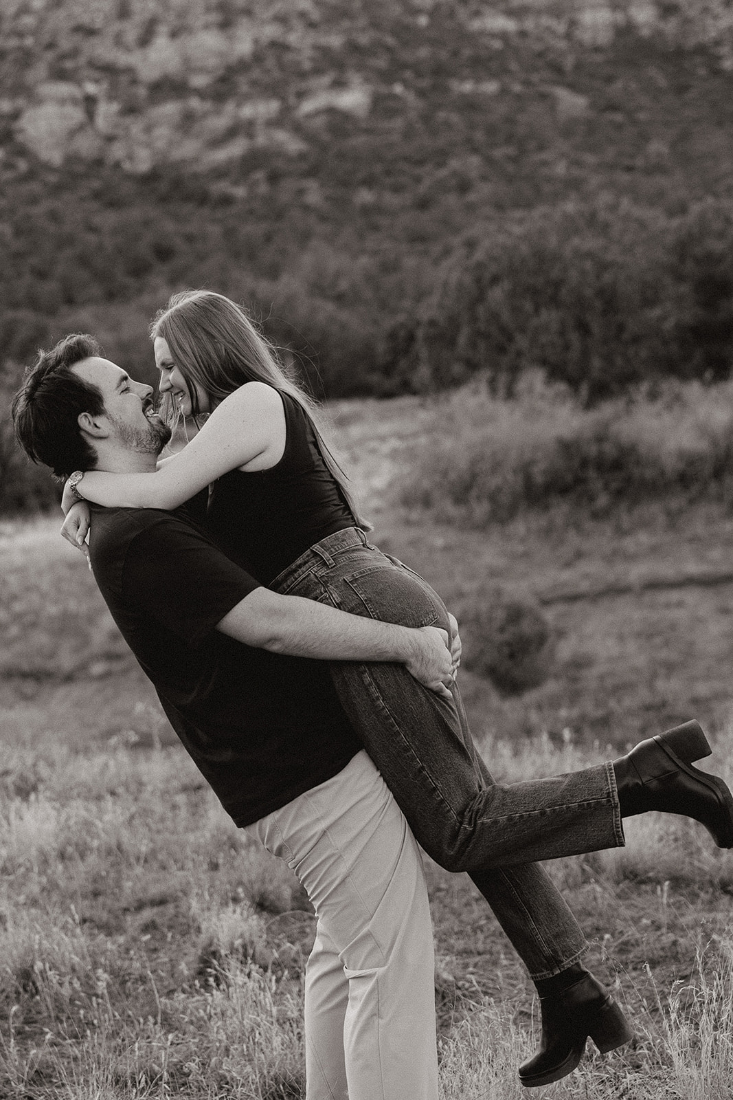 Man lifts his fiance up and holds her before kissing her in black and white portrait