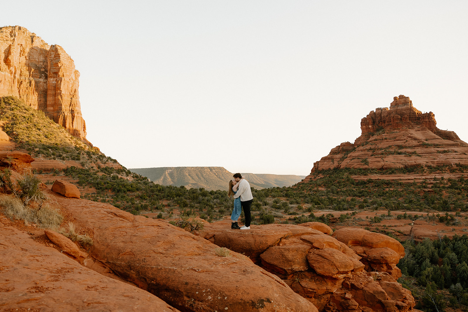A couple stands wrapped in each other on red rock cliffs, surrounded by vast desert views during their Sedona elopement.