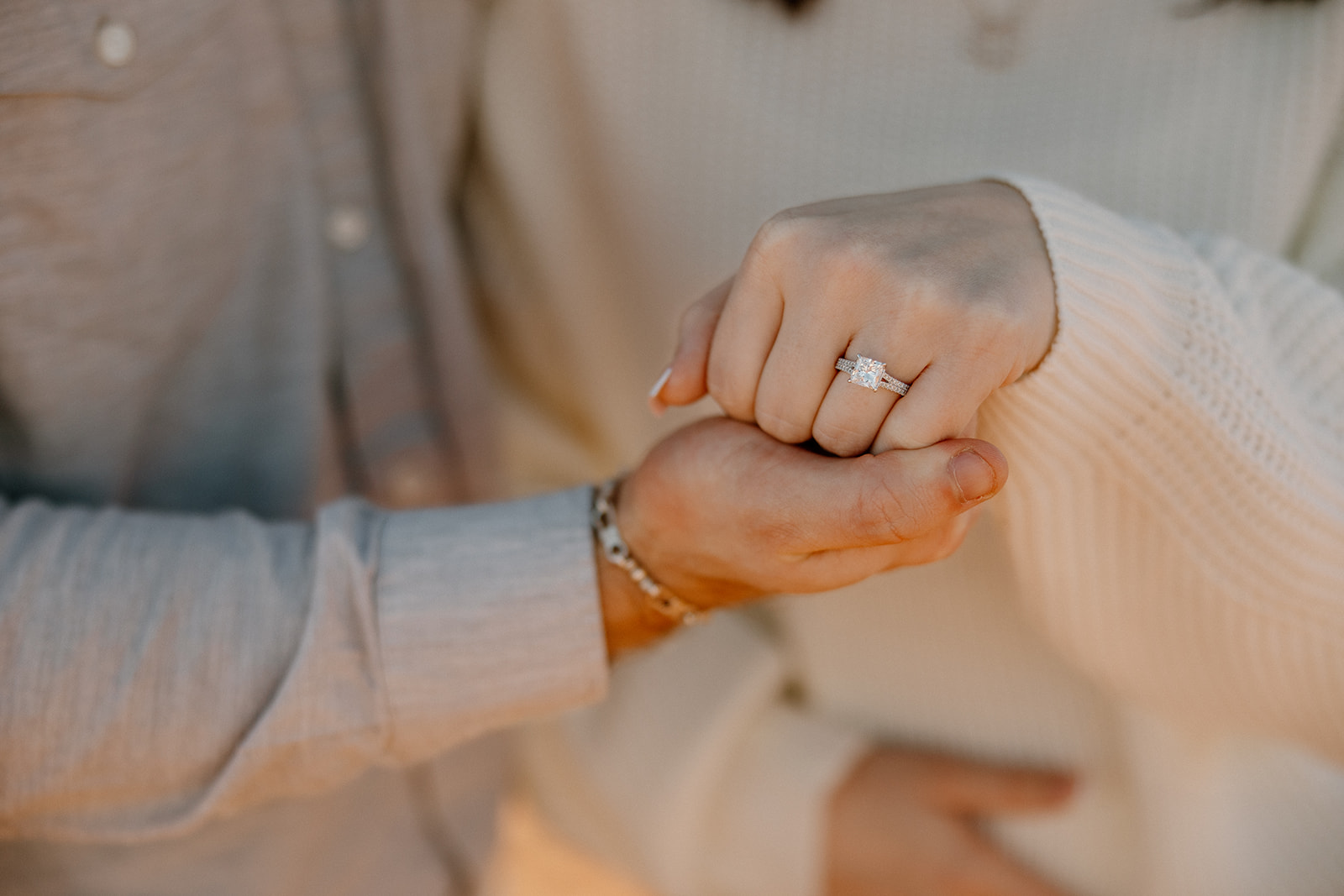 A close-up of the bride-to-be’s hand shows off a radiant-cut engagement ring, held gently by her partner.