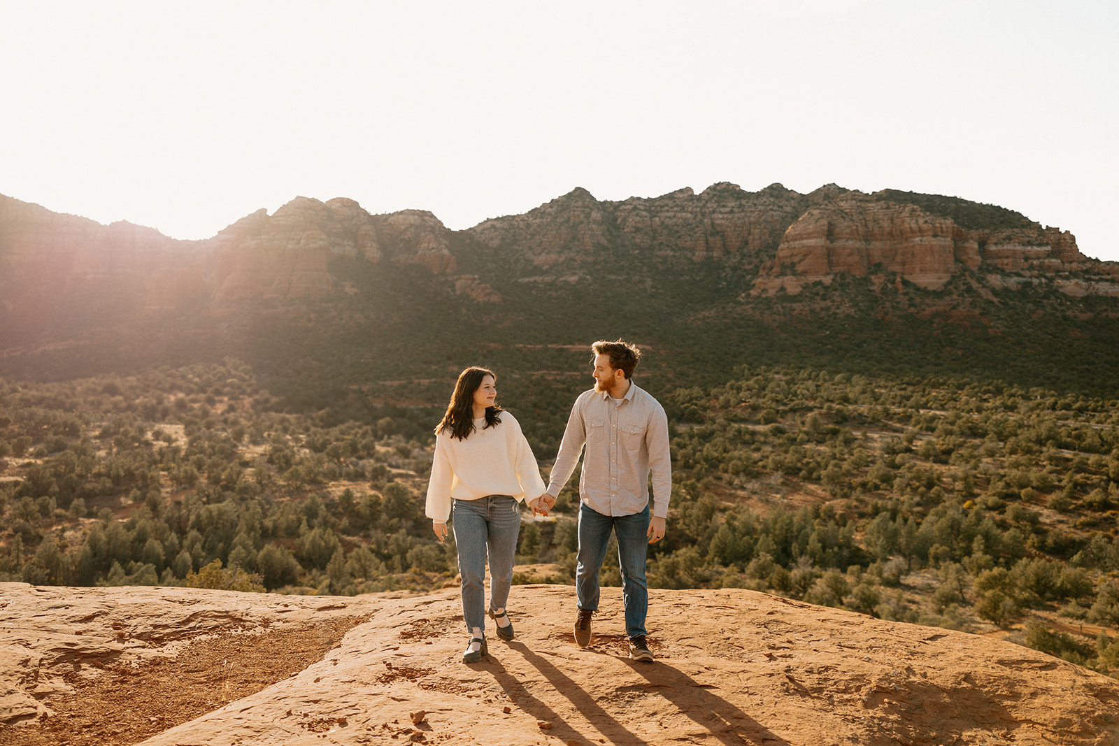 Casual and cozy, the couple strolls across the Sedona cliffs with sunlight spilling over the mountain range.