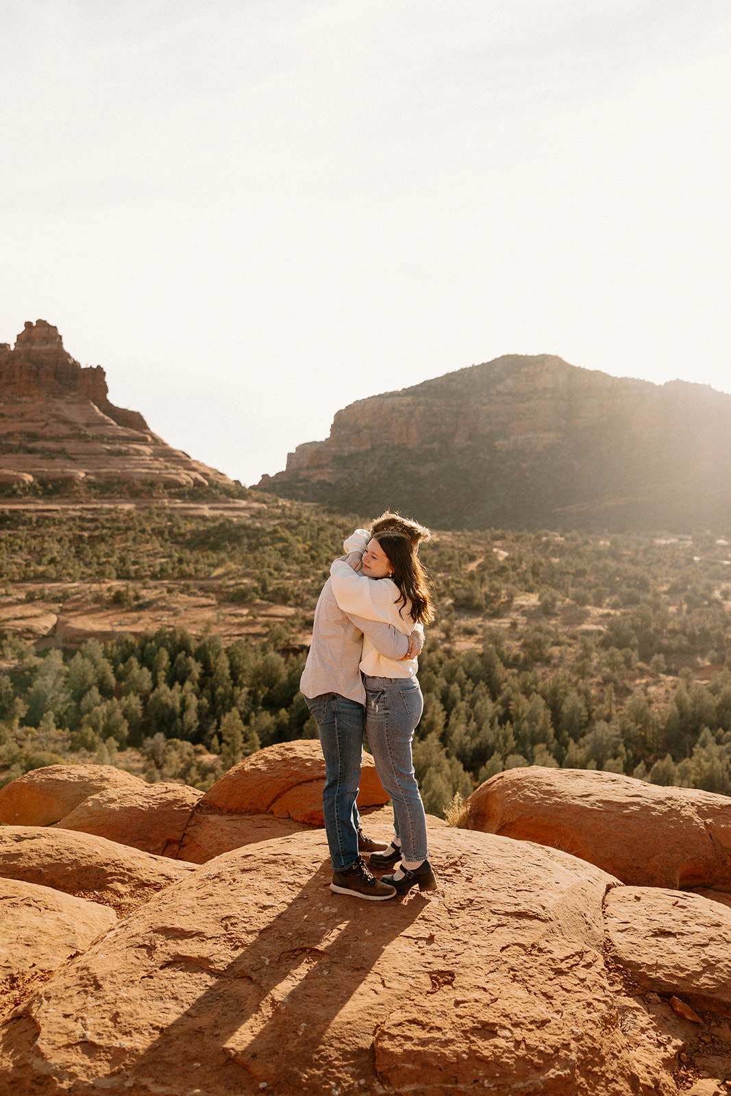 Engaged couple embrace at sunrise atop bright red rocks