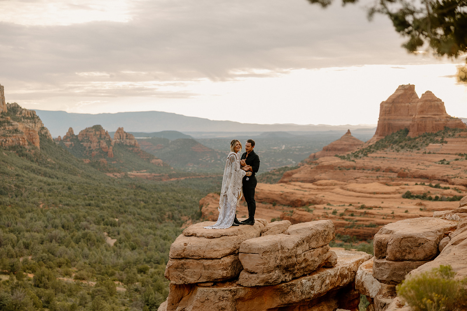 High above the valley, the couple stands on a rock outcrop surrounded by sweeping Sedona views.