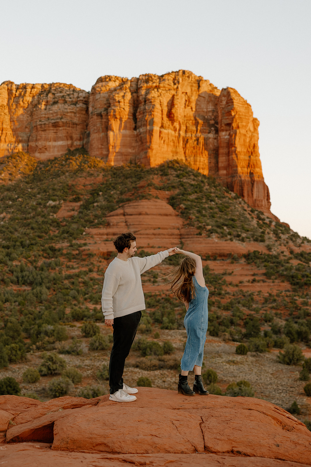 Golden hour glows on Cathedral Rock as he spins her around in a twirl on the red sandstone.