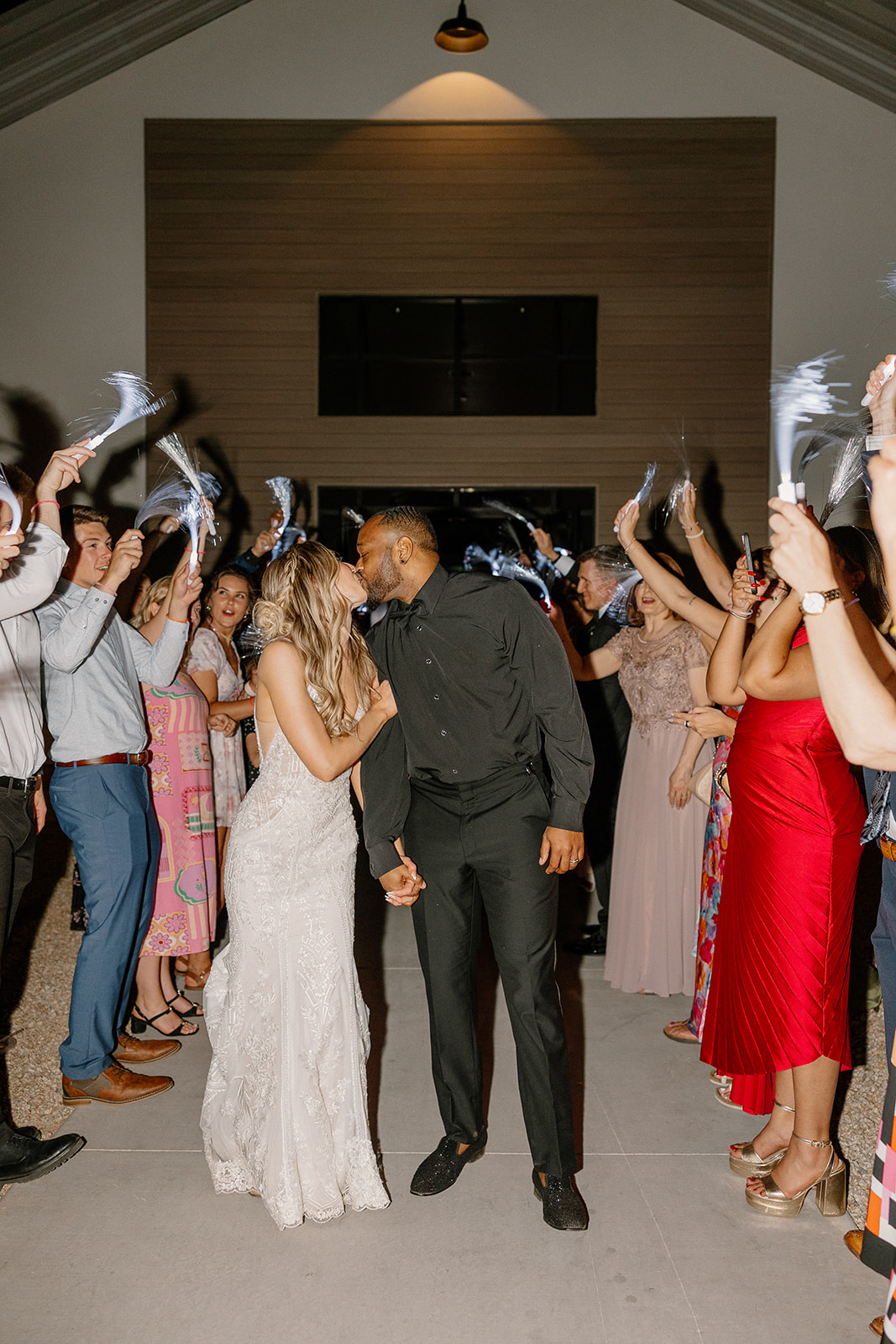 Newlyweds pause for a kiss under a tunnel of glowing fiber-optic wands during their grand exit, wrapped in the magic of desert night air.
