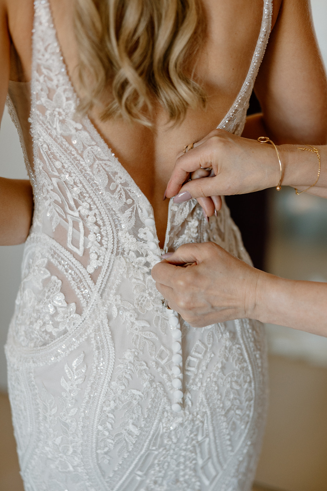 Close-up of delicate hands fastening the bride’s intricate lace gown, every button a love note to the details.