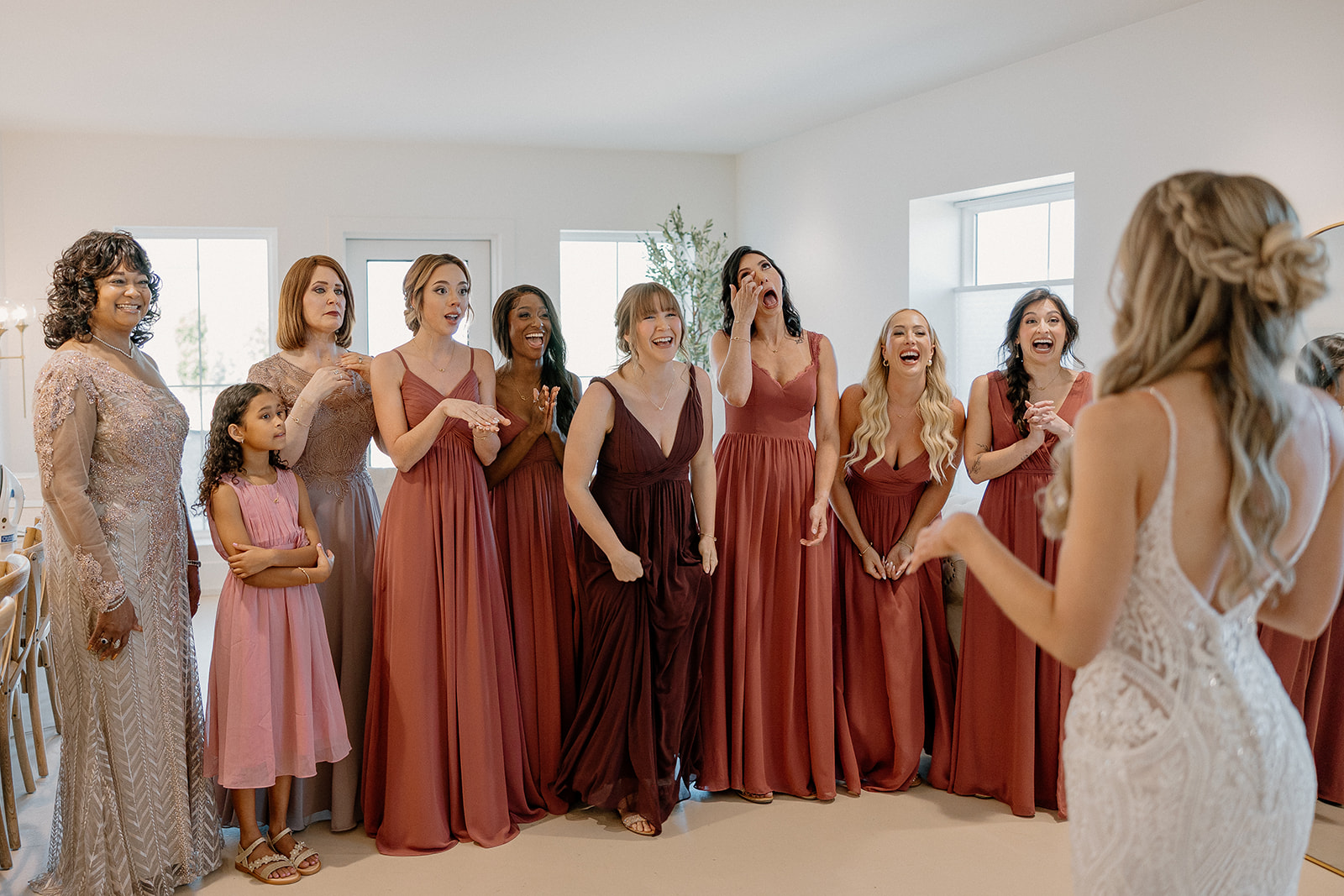 The bride shows off her dress to her bridesmaids and family, whose faces explode with surprise and delight.