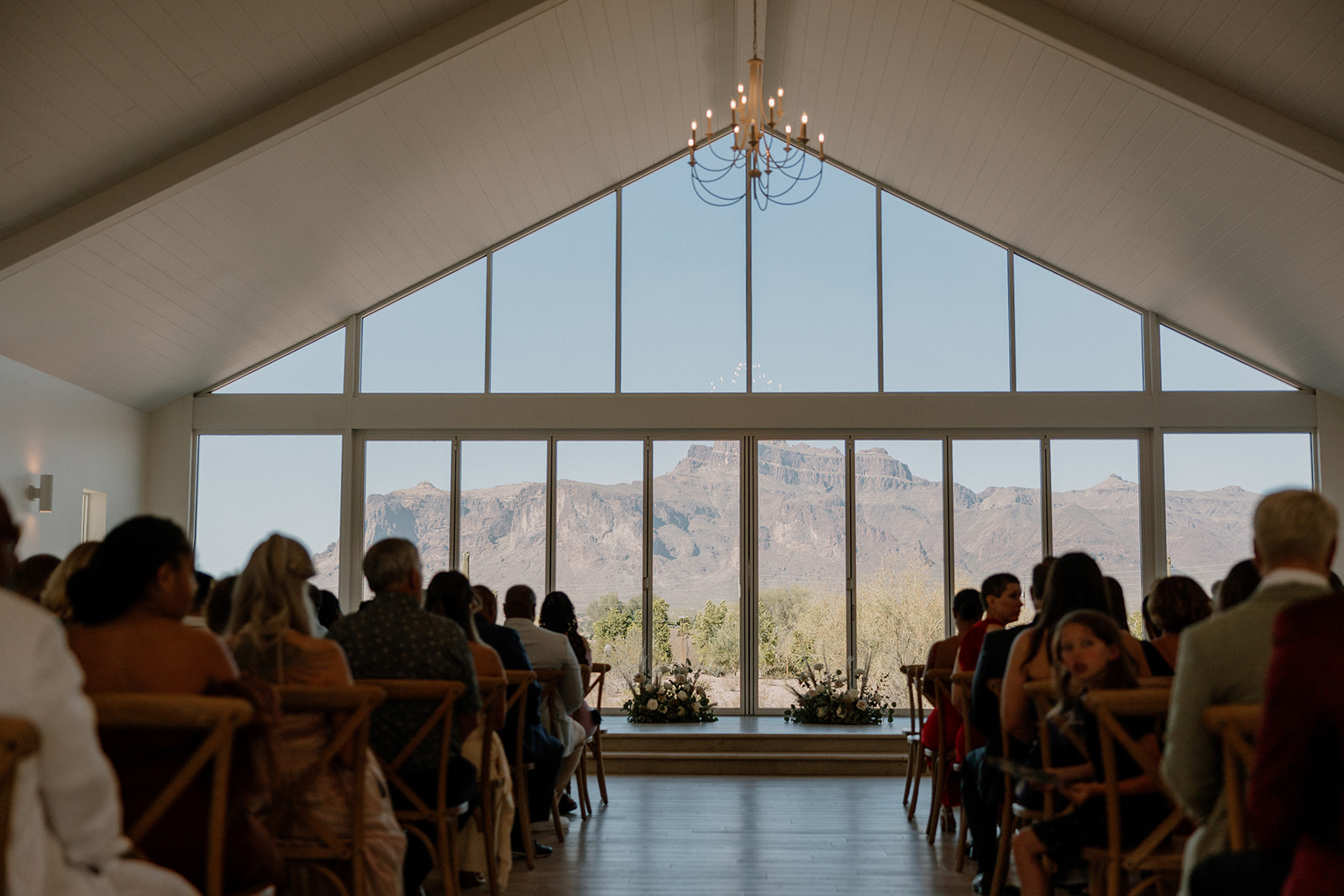 Guests seated inside the chapel face floor-to-ceiling windows framing the Superstition Mountains—an iconic desert view weddings backdrop.