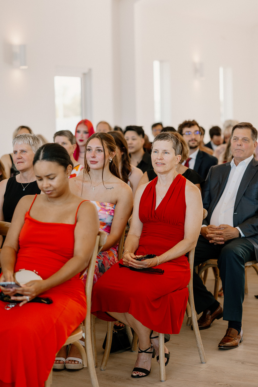 Guests sit attentively in soft neutral light, with bold pops of red and colorful prints adding life to the indoor ceremony space.