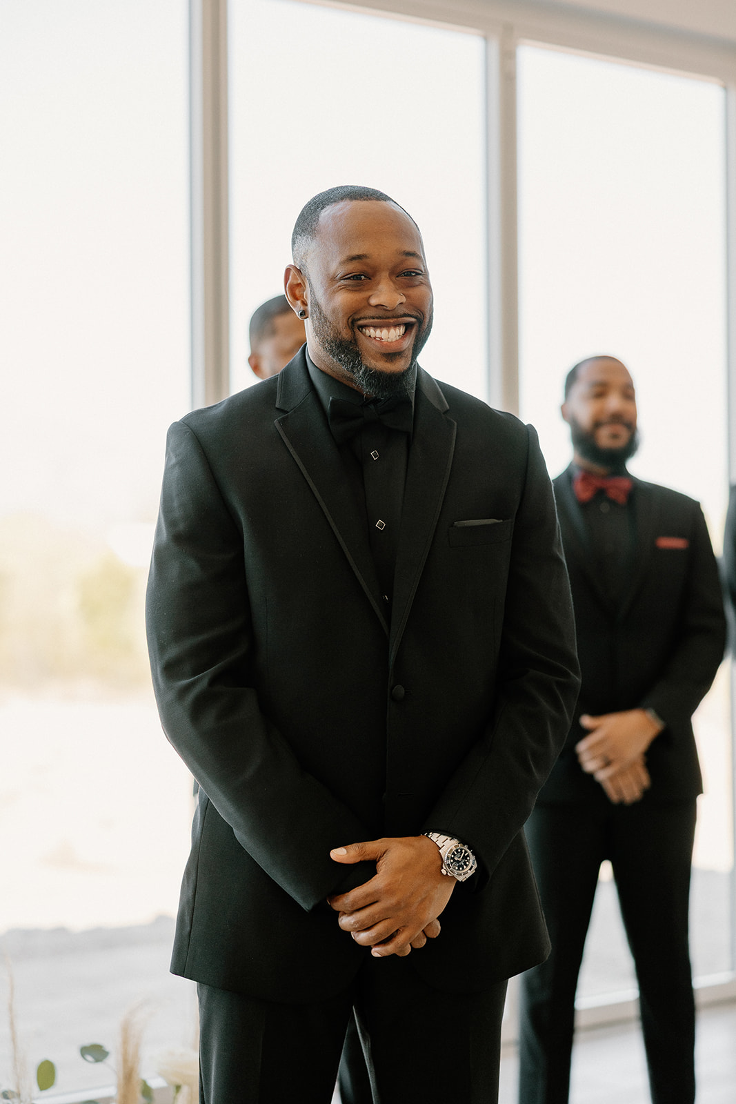 The groom smiles wide, eyes locked on his bride during the ceremony—pure, unfiltered joy under sun-drenched windows.