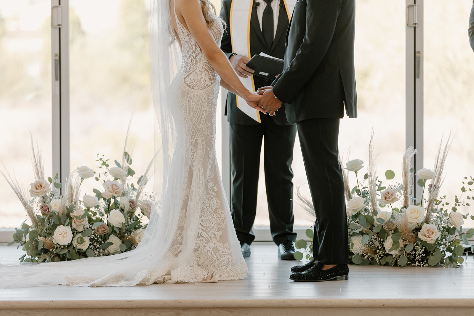 A detailed close-up of the couple’s hands as they exchange vows, surrounded by neutral florals and soft natural light.