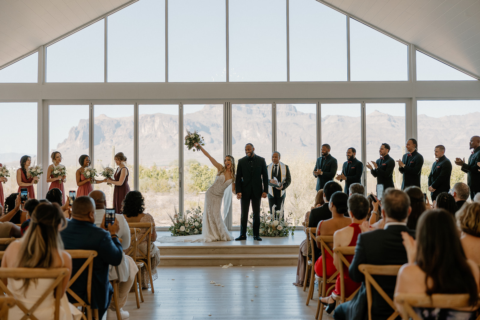 Just pronounced, the bride raises her bouquet high beside her groom at the altar—Superstition Mountains and all the desert view weddings drama on full display.