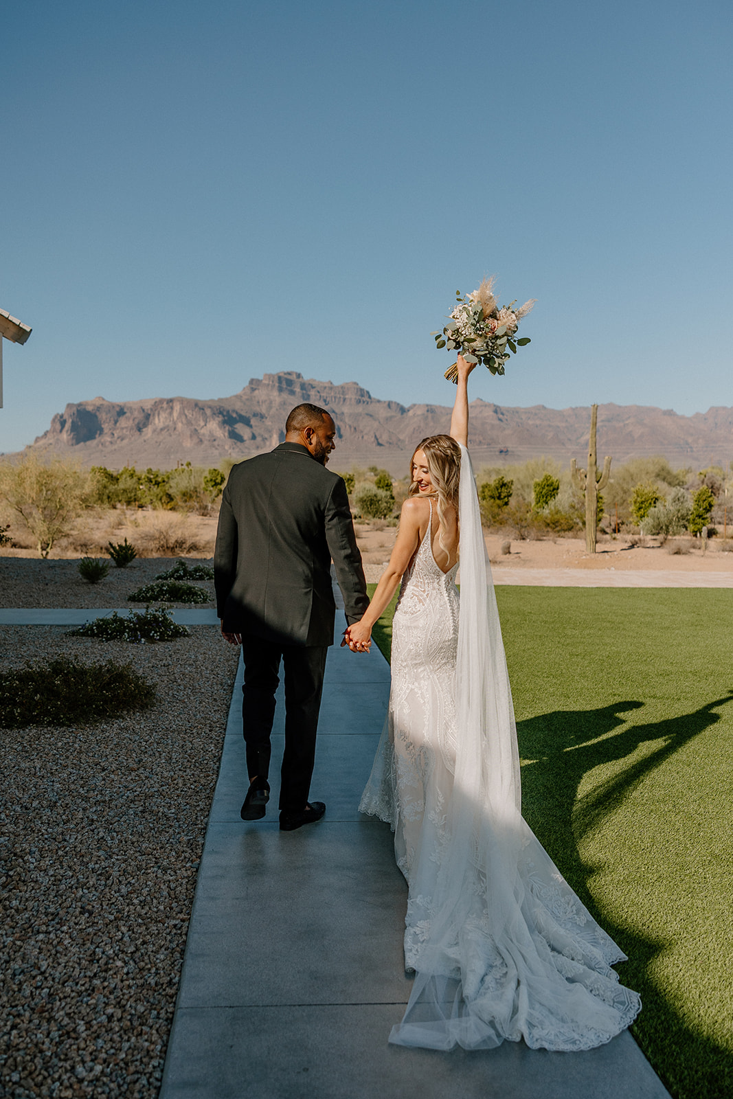 Bride lifting bouquet in the air celebrating recent marriage while holding the hand of her husband after their Desert View Weddings