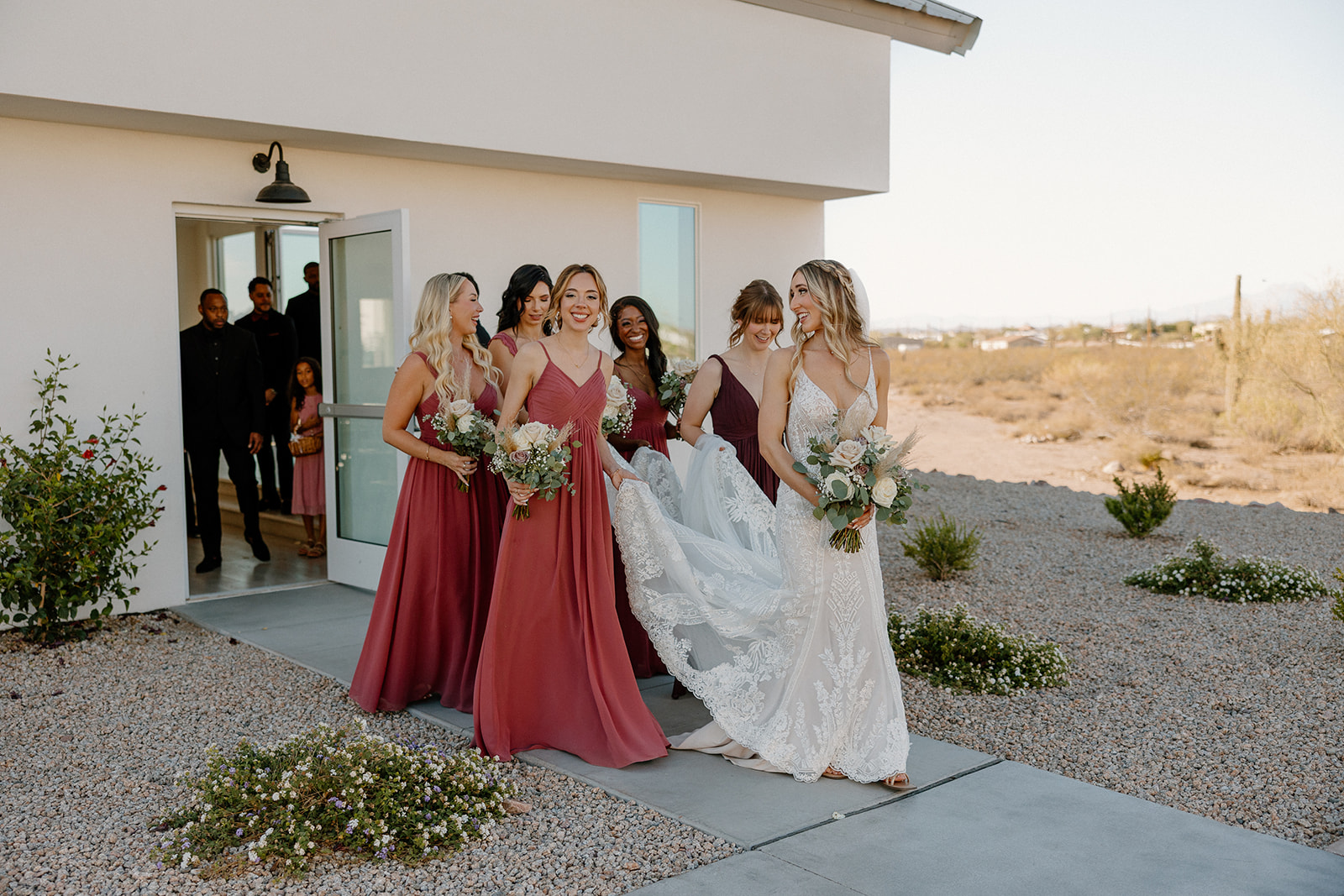 The bride and her bridesmaids step out into the golden desert light, gowns flowing and bouquets in hand—desert views, big energy, zero stress.