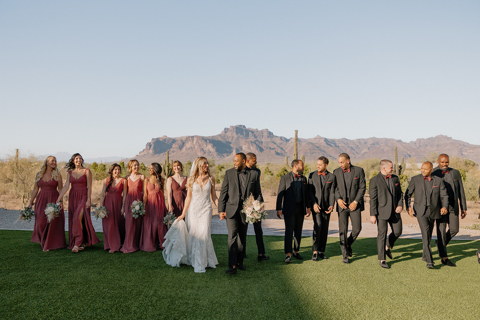The full wedding party walks in unison with Superstition Mountain in the backdrop—sunlit florals, moody tones, and sweeping views at this desert view weddings location.