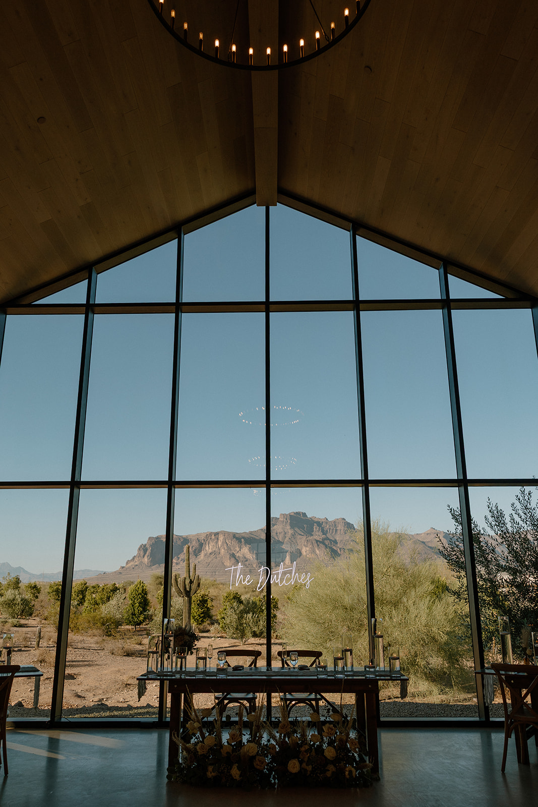 Sweetheart table in front of windowpanes with the couple's married name in an LED sign and mountains behind it