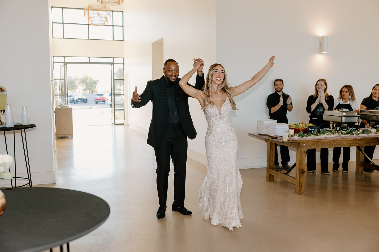 Hands lifted in triumph, the couple makes their grand entrance to a cheering crowd—energy high and hearts full at their Arizona celebration.