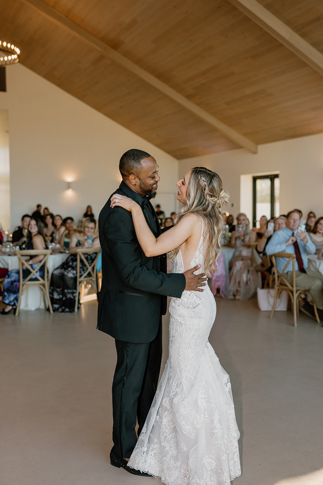 Bride and groom share their first dance beneath wooden beams and golden light, surrounded by smiling guests at this desert view weddings reception.