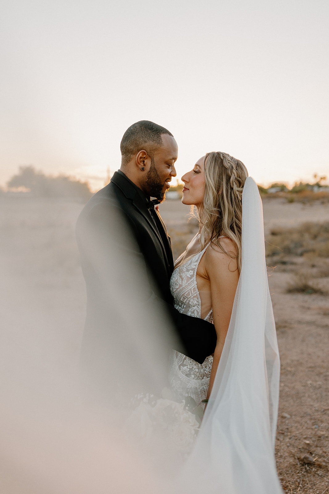 Bride's veil blows in the wind as groom brings her in close to embrace after their intimate wedding