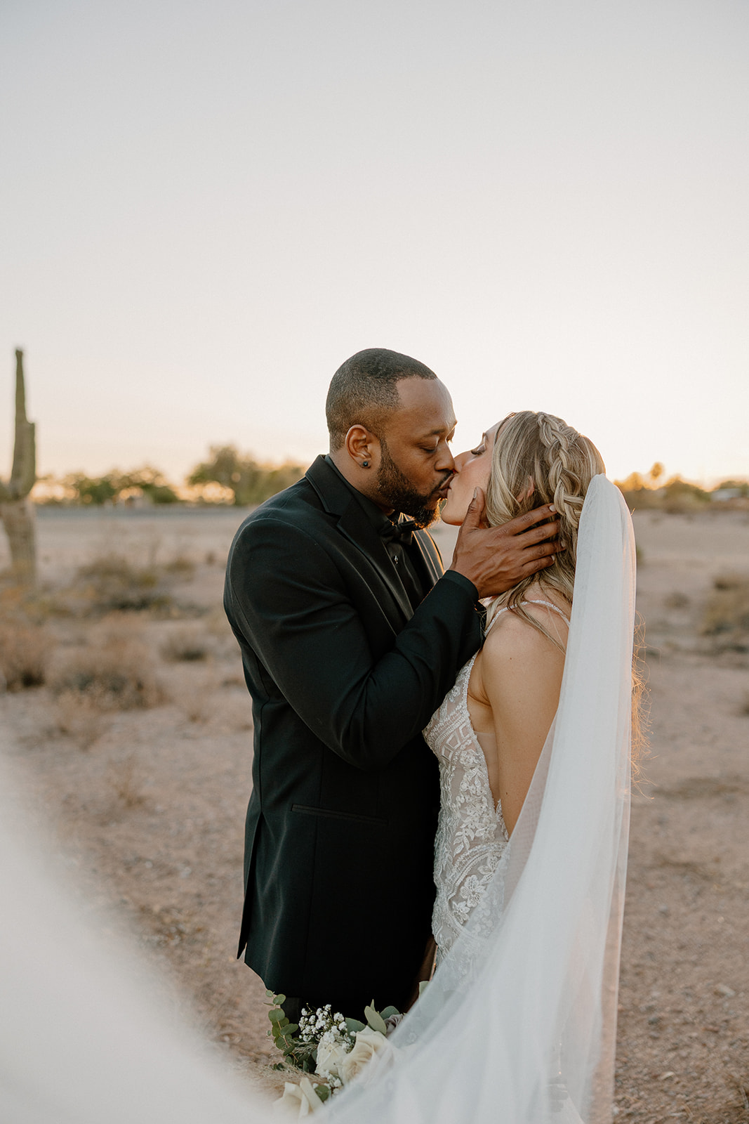 With soft evening light and desert textures around them, the groom pulls his bride close for a forehead kiss that says everything.