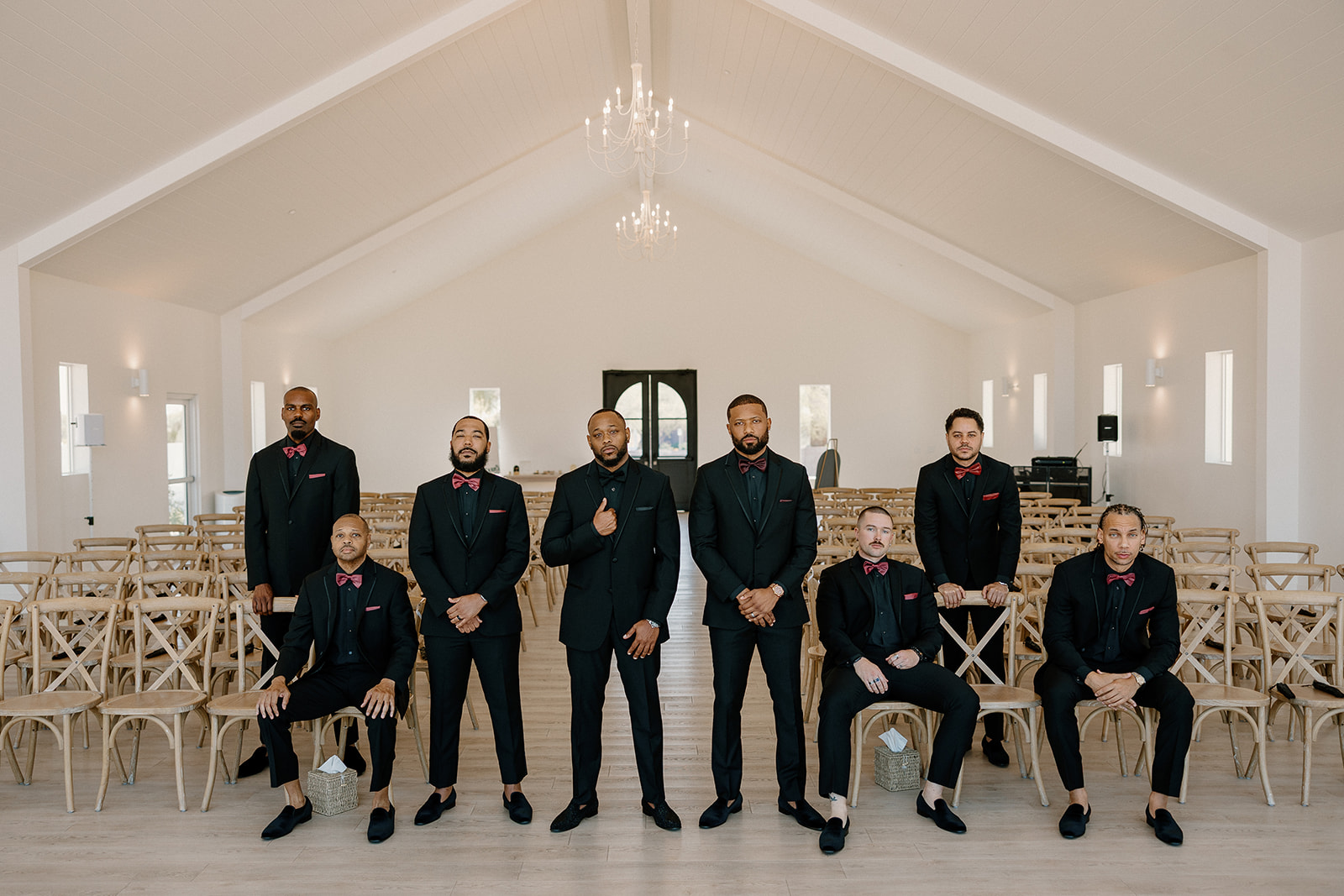 The groom and his groomsmen pose inside a minimalist white chapel, dressed in all black with burgundy accents—elevated style for this desert view weddings crew.
