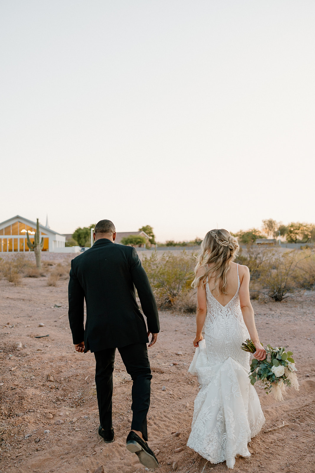 The couple walks side-by-side through the open desert, footsteps trailing behind them as they head into the soft Arizona dusk.