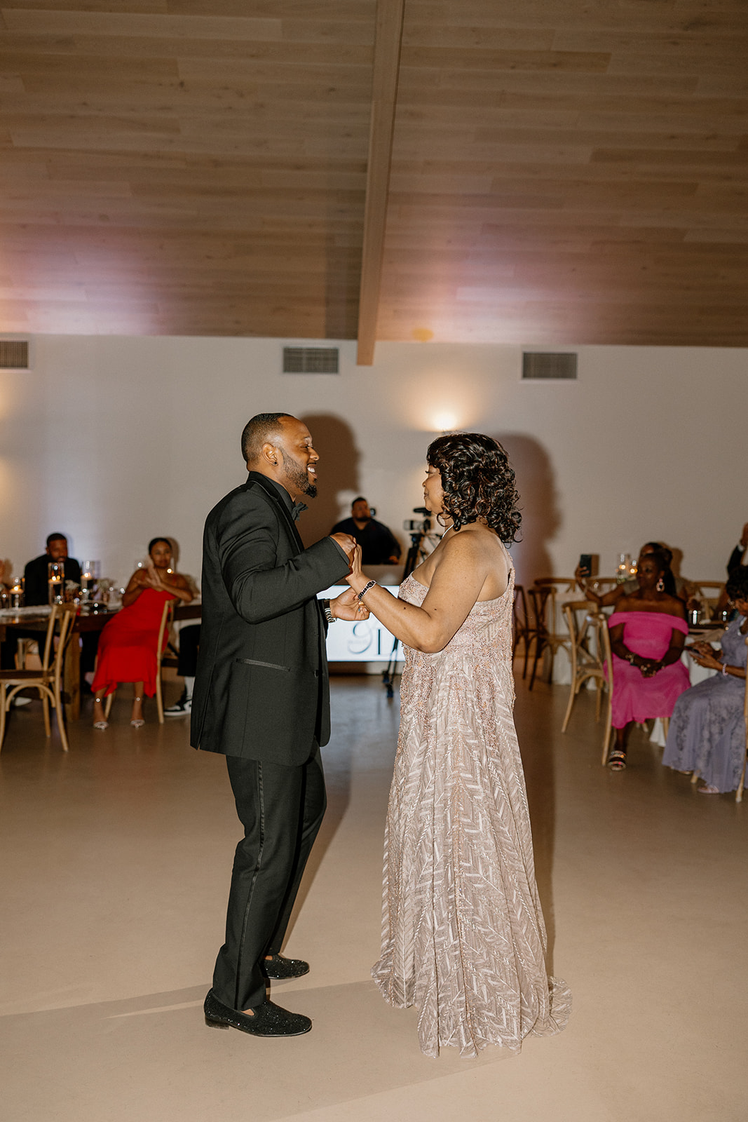 The groom shares a sweet, quiet moment with his mother during their special dance, the soft lighting wrapping them in intimacy and warmth.