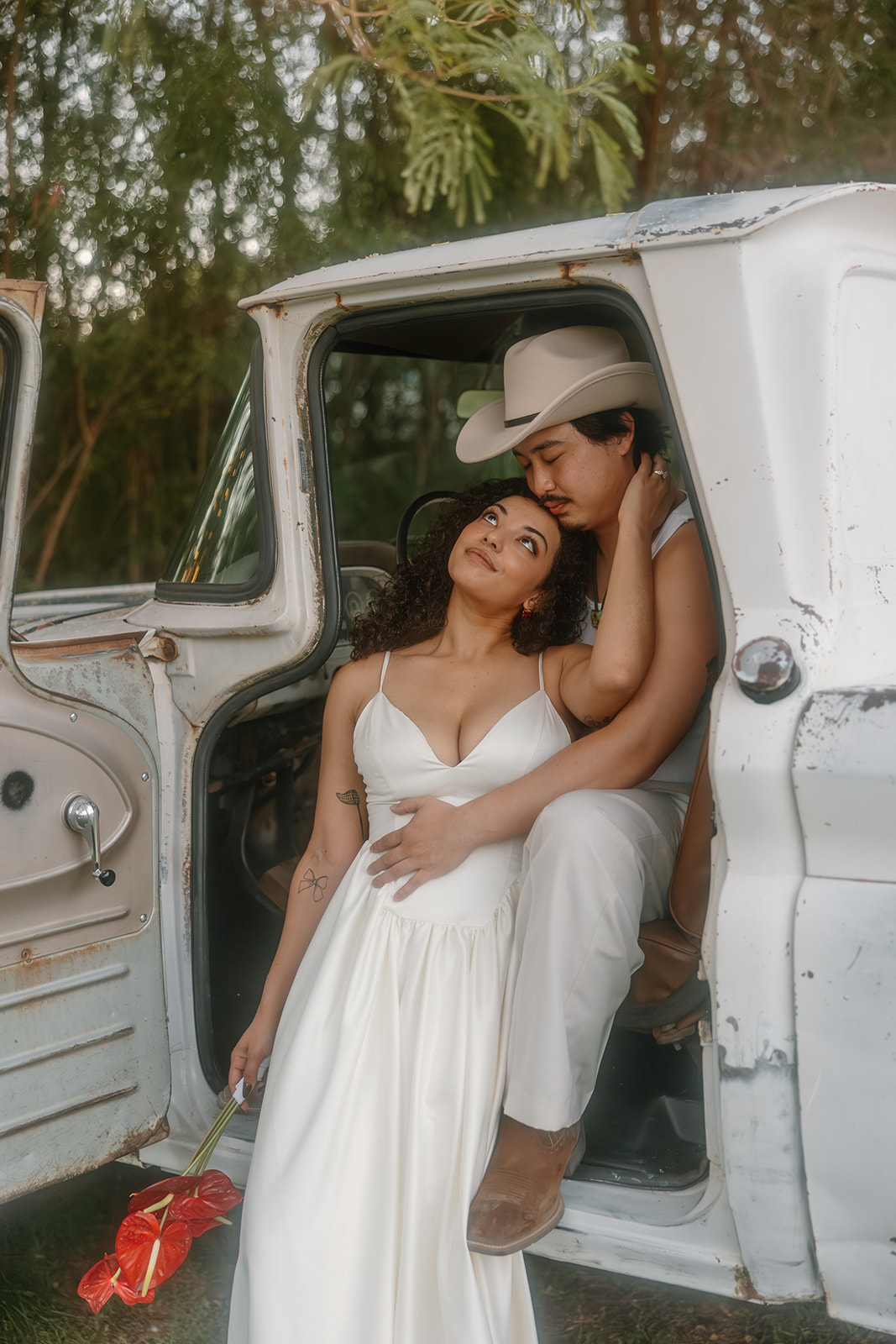 The couple sits inside an old white truck, the groom wrapping his arms around the bride as she leans against him holding a bouquet—Western wedding love captured in a vintage, heartfelt moment.