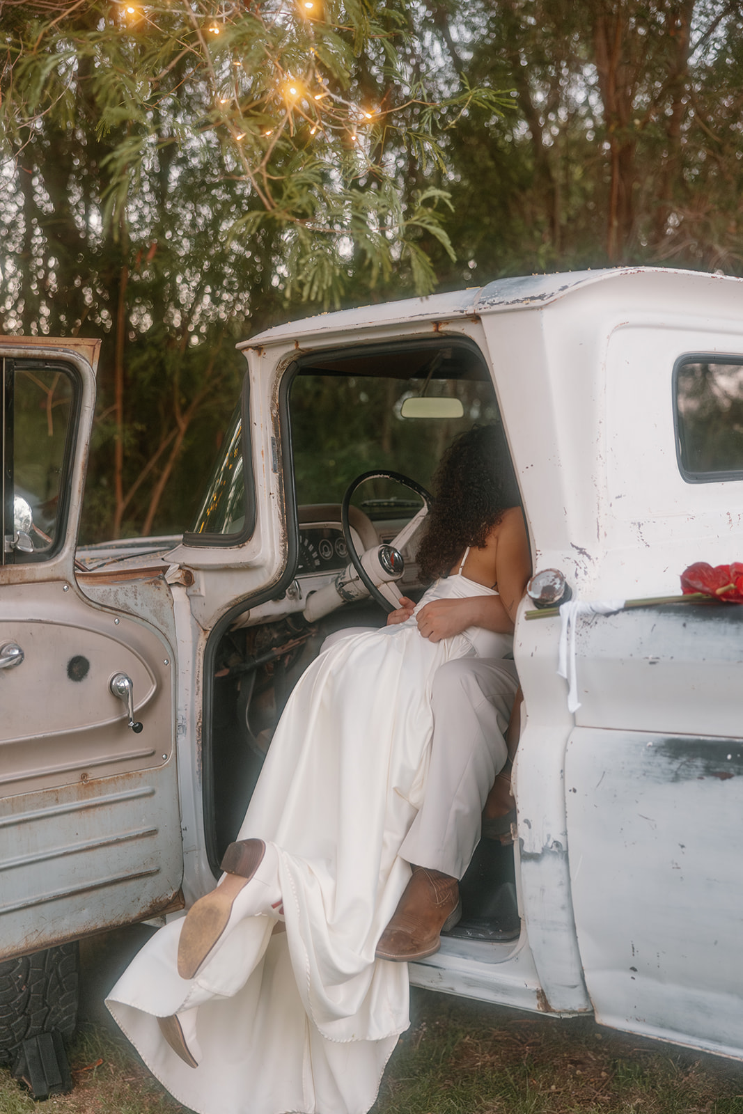 An intimate kiss inside the open door of the rustic white truck. The bride leans into the groom's lap as they share a quiet moment, surrounded by the soft light of string lights.