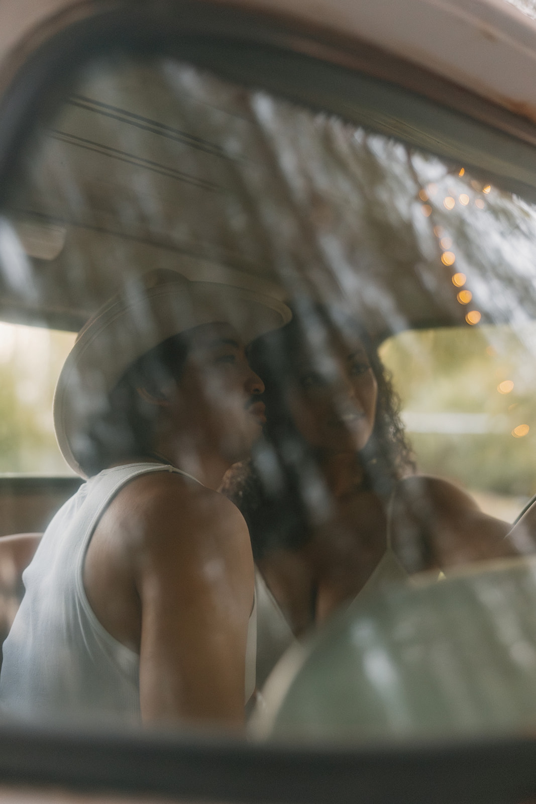 Shot through the truck window, the bride and groom sit close inside, their silhouettes softened by reflections of twinkle lights and trees—an intimate Western wedding moment.