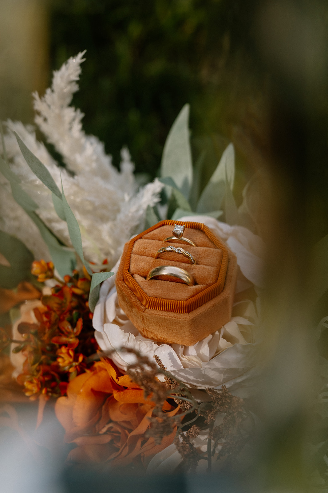Three wedding rings displayed in a rust velvet box nestled in an autumn-inspired bouquet.