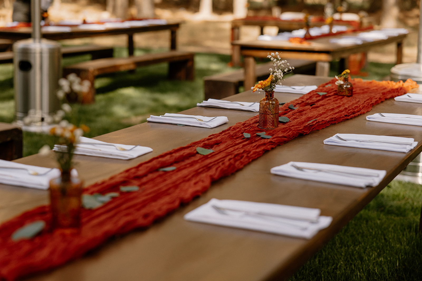 Close up of reception table set up with rust colored table runner, greenery and small centerpieces for a minimalistic setup. 
