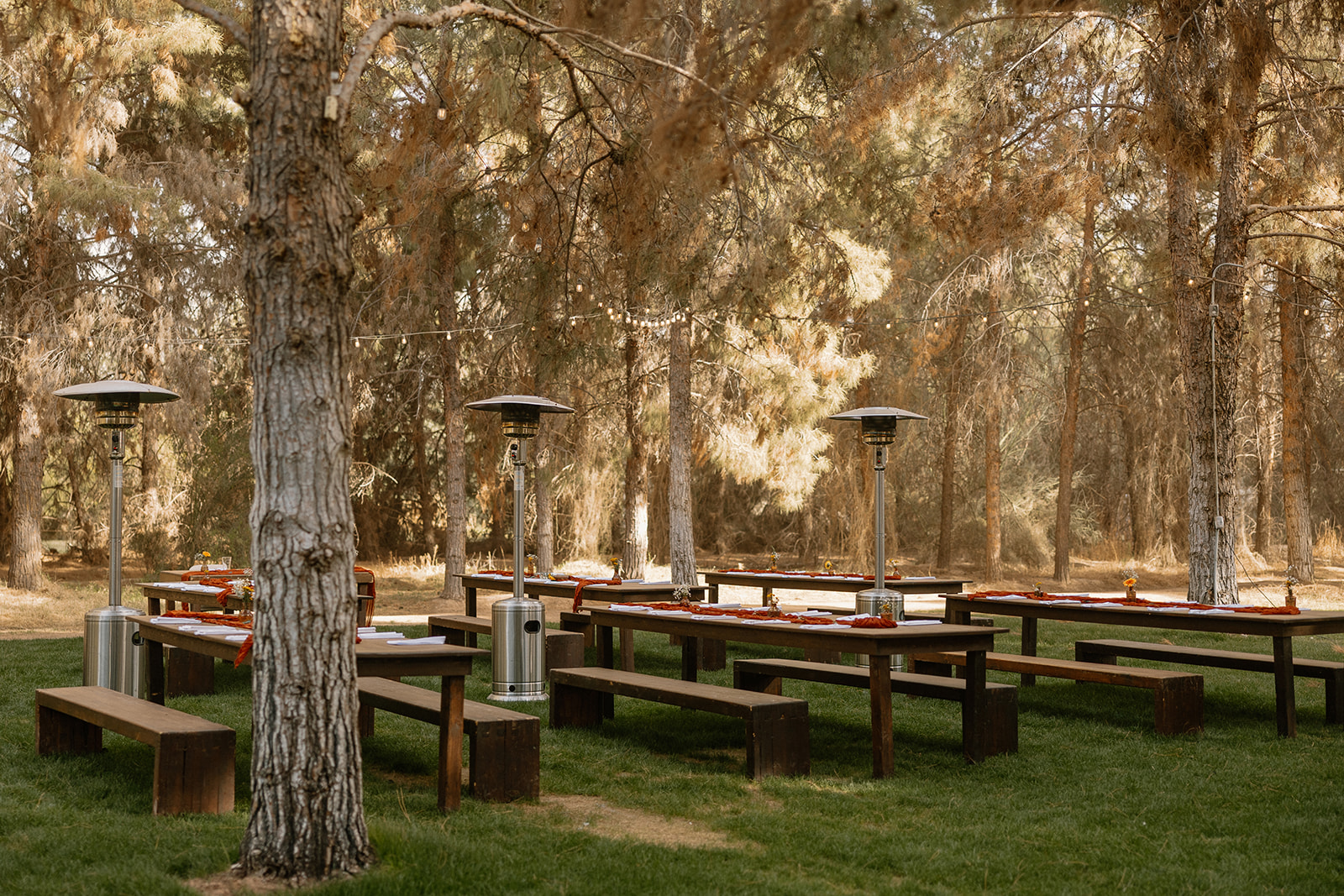Outdoor wedding reception set up with wooden tables, rust colored napkins and heaters.