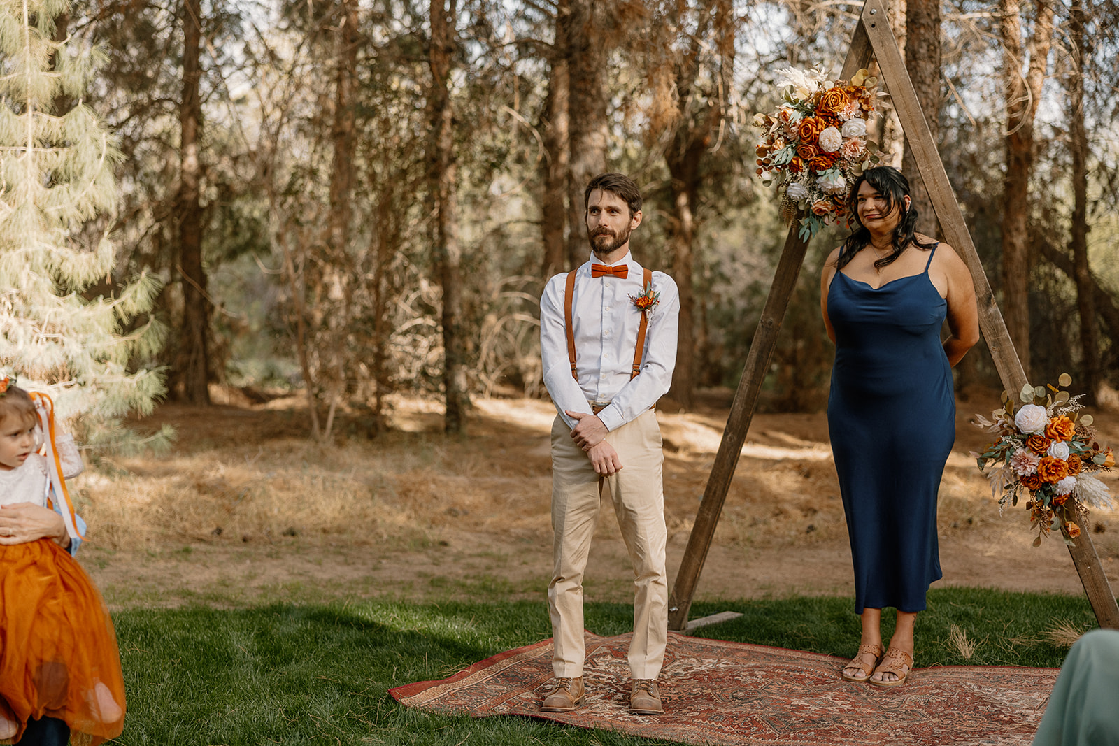 Groom stands at the altar under a triangle floral arch with his officiant, waiting for the ceremony to begin at Schnepf Farms.
