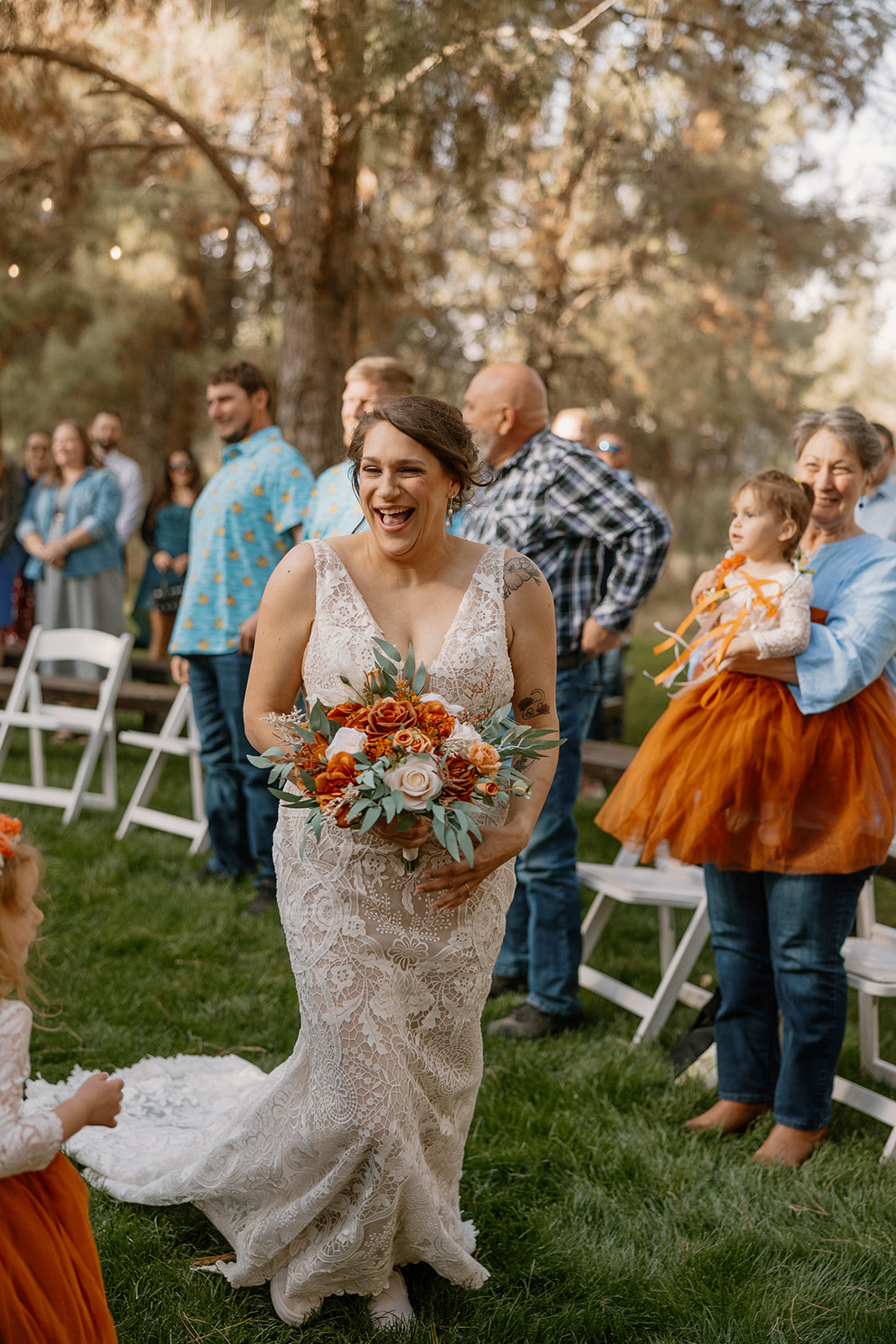 Smiling bride holding a bold bouquet walks down the aisle lined with guests and flower girls at Schnepf Farms.