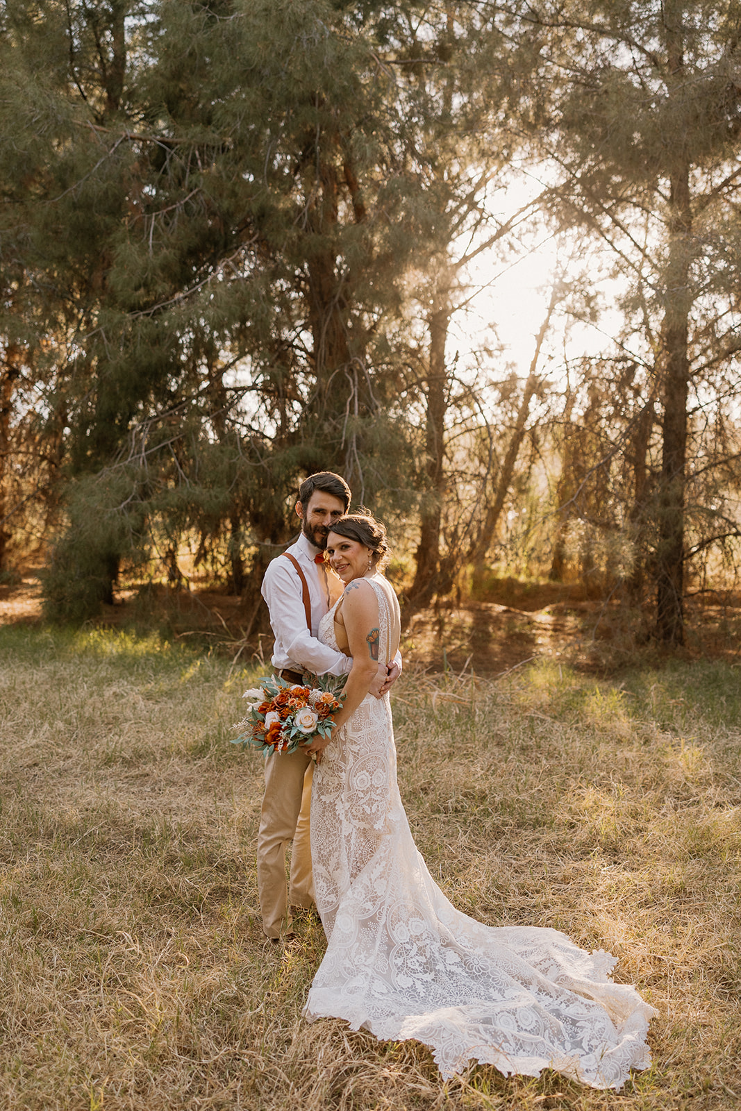 Bride and groom embrace in a grassy field as golden light filters through the trees at Schnepf Farms.
