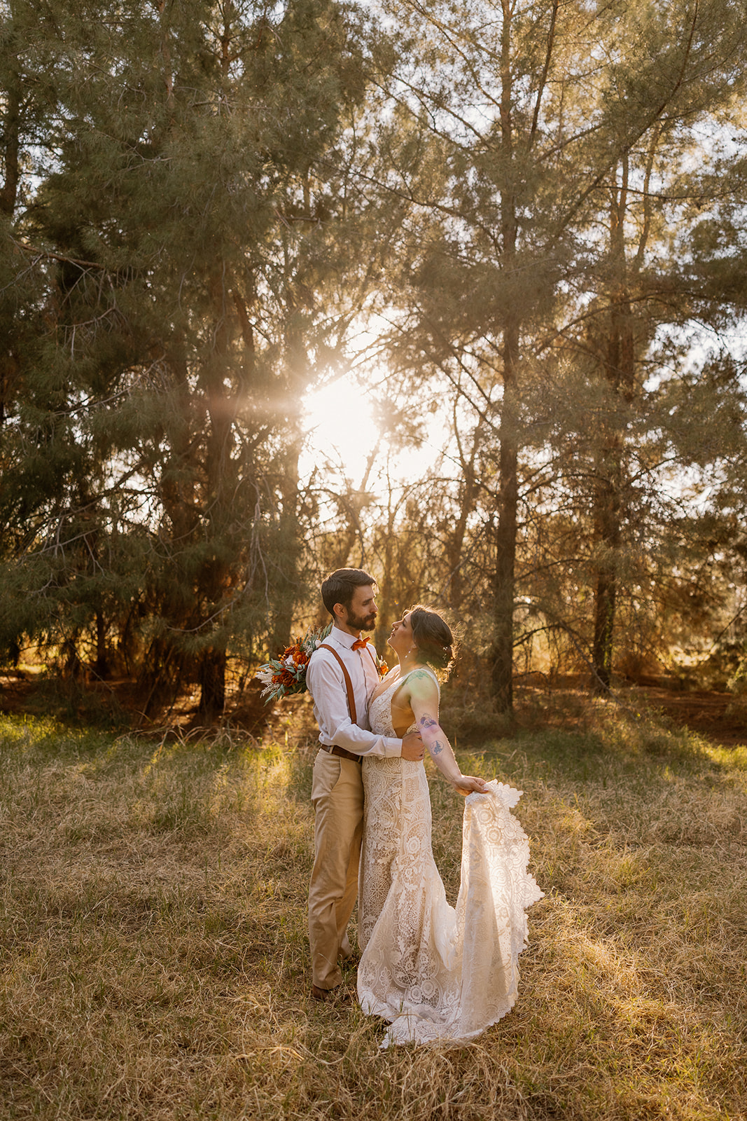 Bride and groom taking golden hour portraits as sun peeks through the trees. 