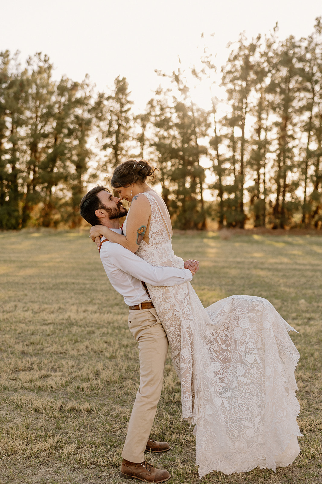 Groom lifts his bride off the ground for a romantic kiss at golden hour in the open fields of Schnepf Farms.