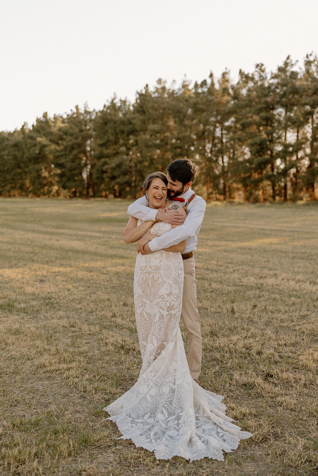 Groom embraces bride from behind making her laugh and smile during bridal portraits. 