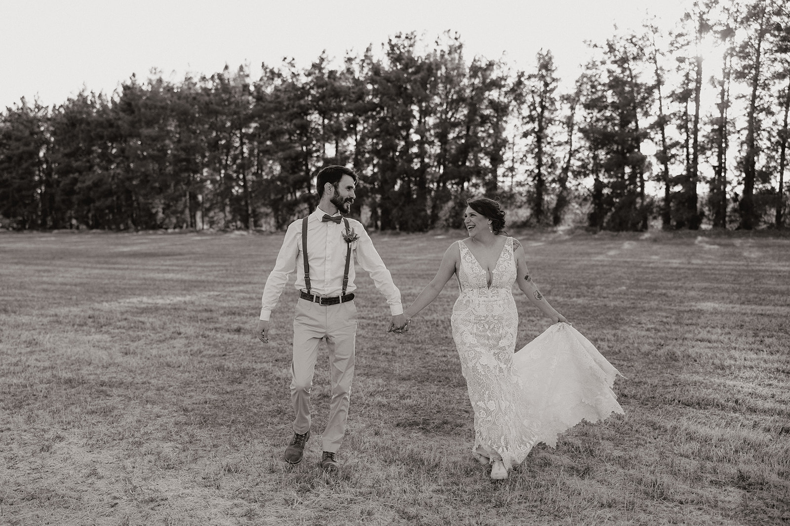 Newly married couple holding hands and walking together through grassy field laughing and smiling together. 