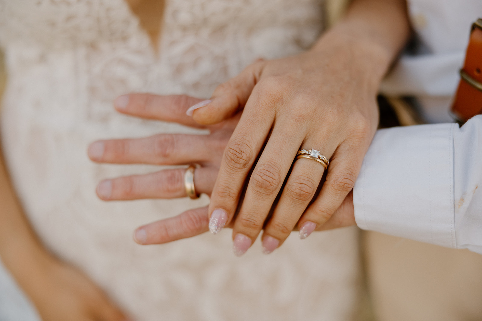 Close-up of newlyweds’ hands displaying their gold wedding bands and engagement ring after saying “I do.”