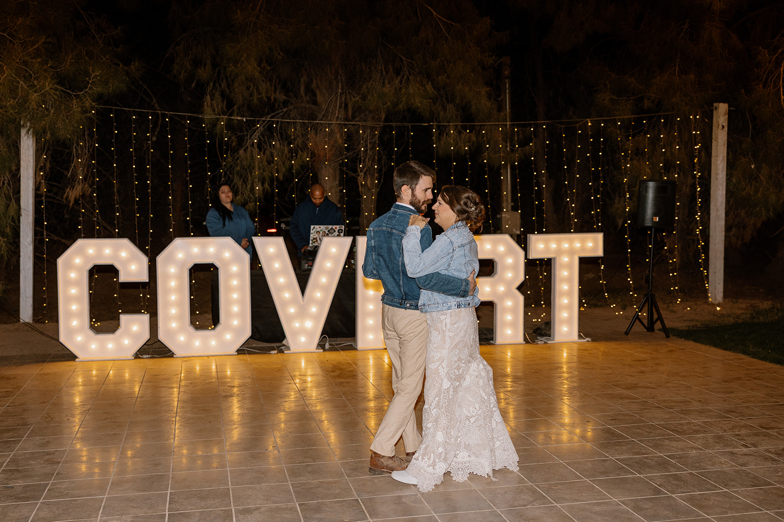 Newly married couple dance during first dance as husband and wife in front of neon letter signs spelling out their new last name. 