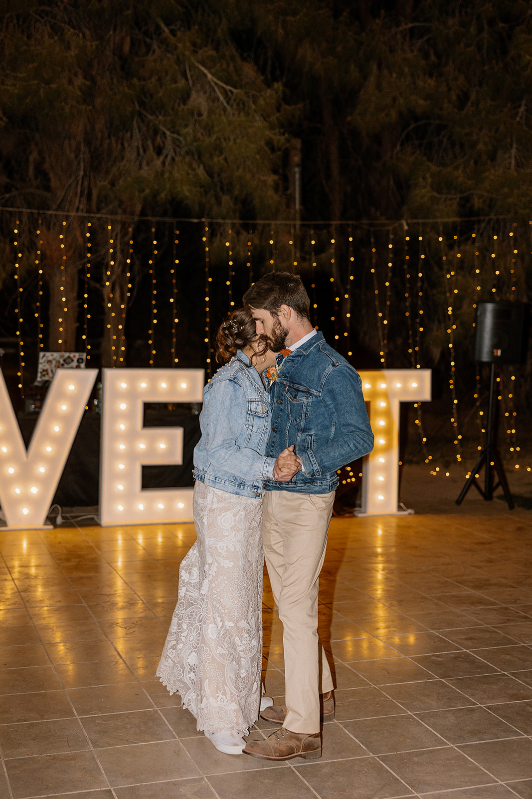 Bride and groom dance under twinkle lights and a glowing “LOVE” sign during their Schnepf Farms wedding reception.