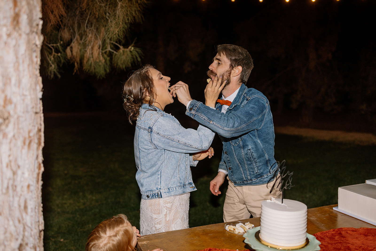 Couple feeds one another bites of wedding cake at outdoor reception