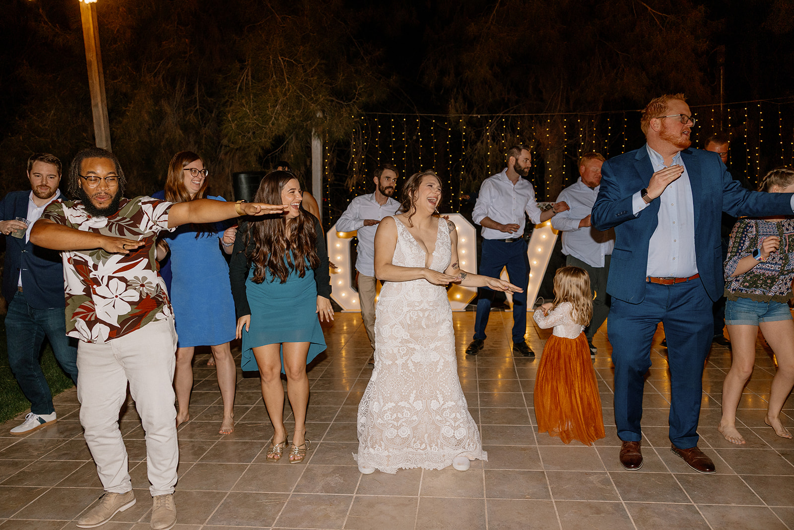 Couple dances with wedding guests on dance floor having fun and laughing together. 