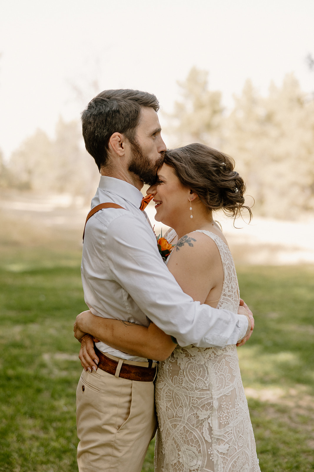 Groom kisses bride on the forehead as they hold each other close, caught in a quiet, emotional moment.