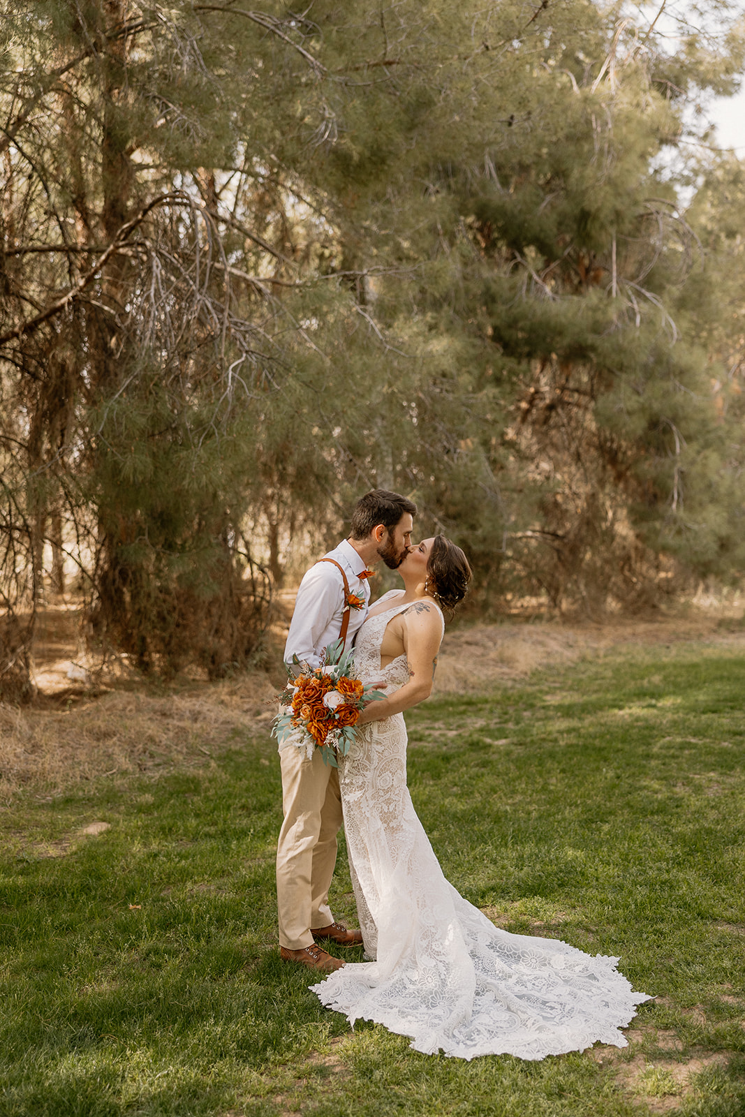Bride and groom share a kiss as the bride holds a bold fall bouquet, surrounded by the greenery of Schnepf Farms.