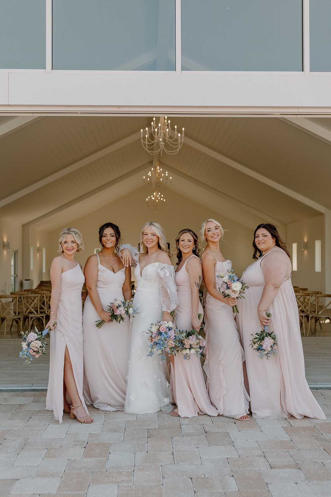 Bride stands with bridesmaids in pink dress outside venue smiling together. 