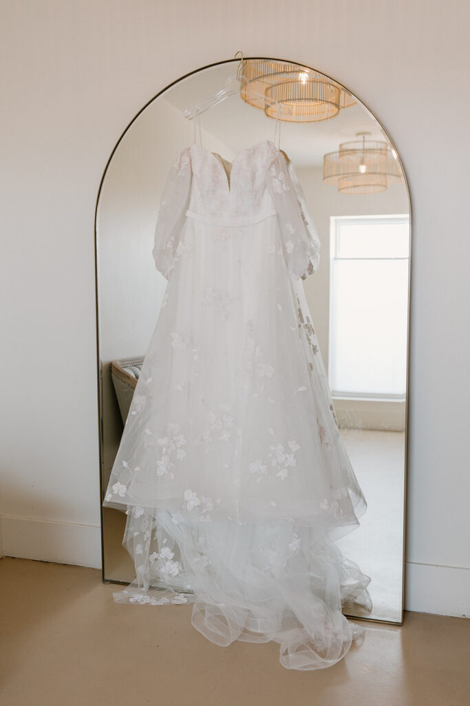 Lacy white wedding gown with long sleeves hanging in front of mirror before Desert View wedding