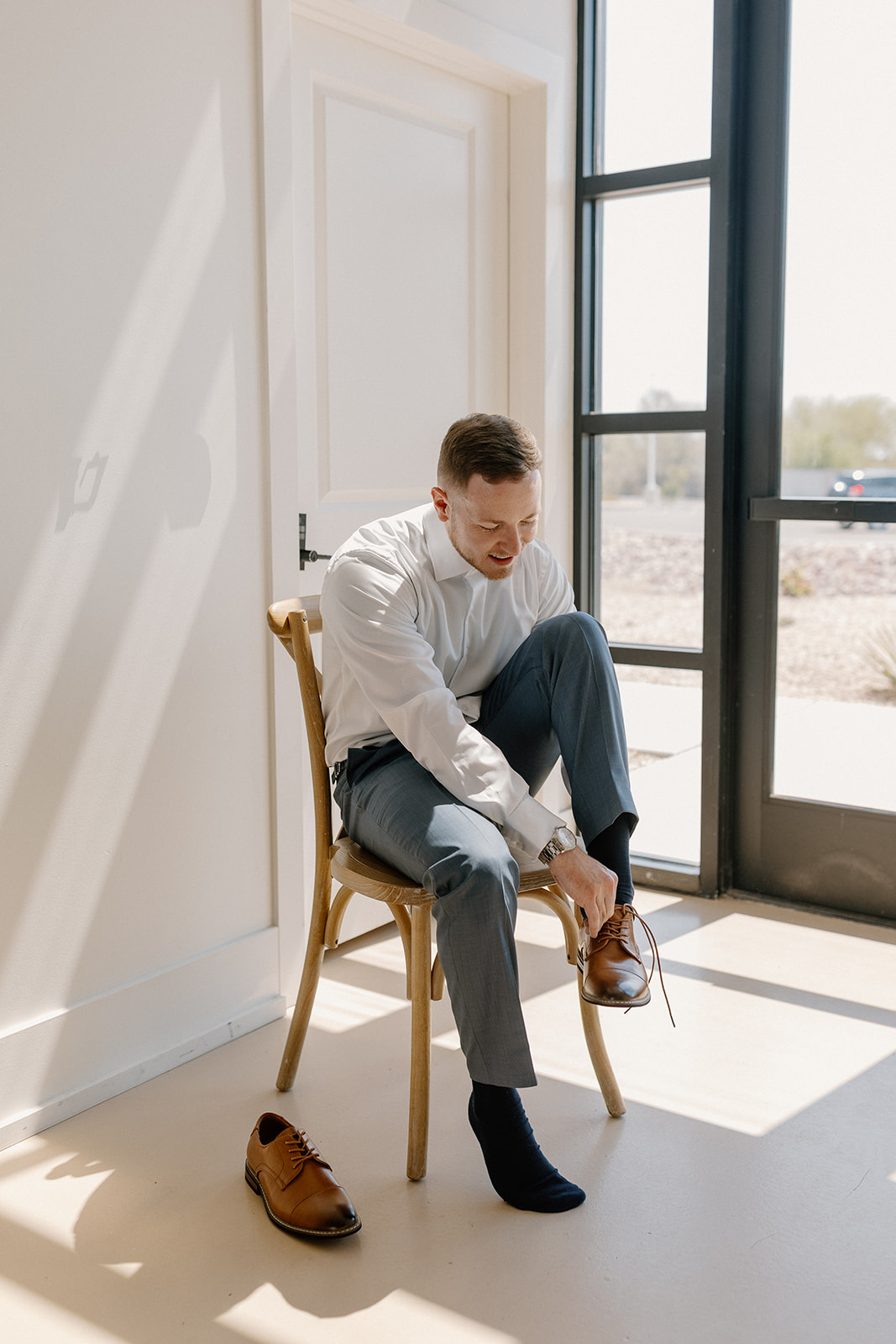 Groom sitting in chair putting on brown dress shoes, getting ready for his big day. 